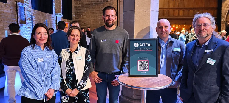 Five members of the AITEAL project team standing beside an AITEAL display at an event